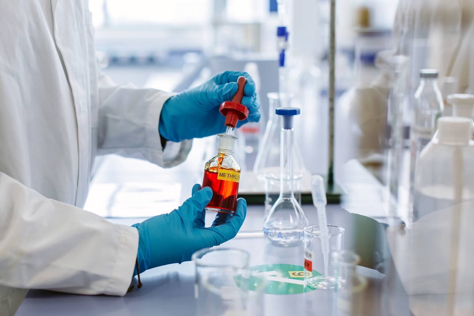 Gloved hands holder glass beakers with orange liquid